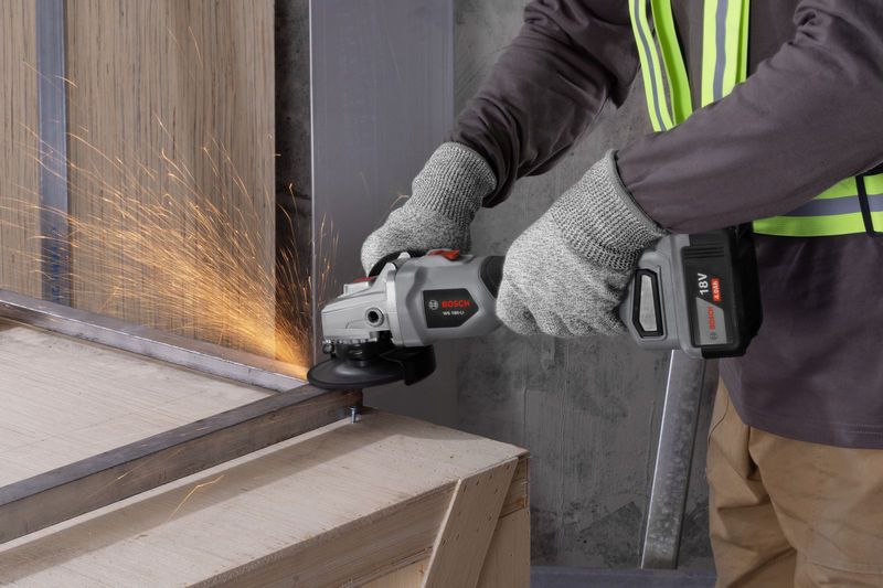 一名佩戴安全设备的人正在研磨金属梁，产生火花。.