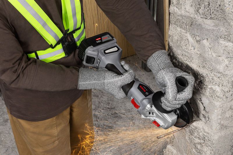 一名佩戴安全设备的人员正在使用无绳角磨机打磨墙壁。.