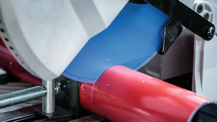 金属切割锯切割固定在夹具中的红色管道。.