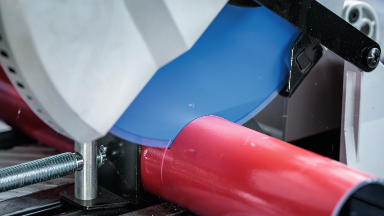 金属切割锯切割固定在夹具中的红色管道。.