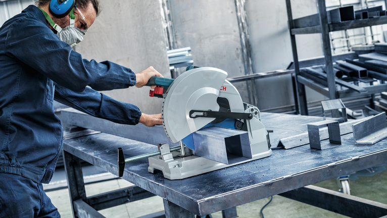 车间里，佩戴安全设备的人员用圆锯切割金属梁。.