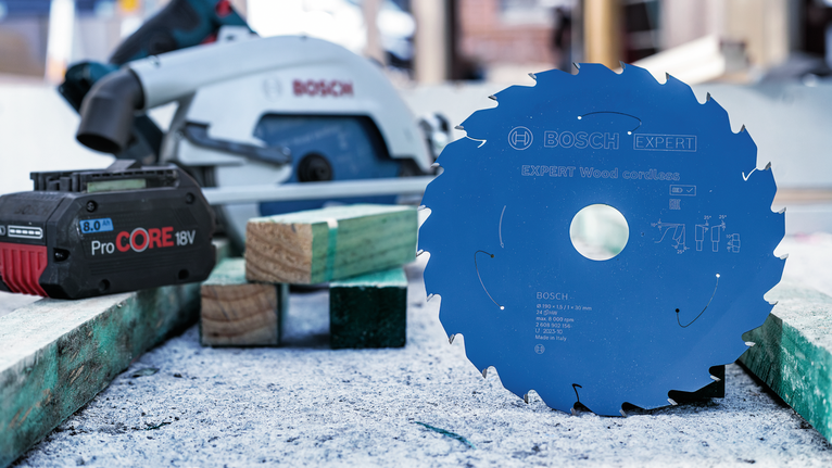 圆锯片直立在工作台上，旁边是无绳电池和锯子。.