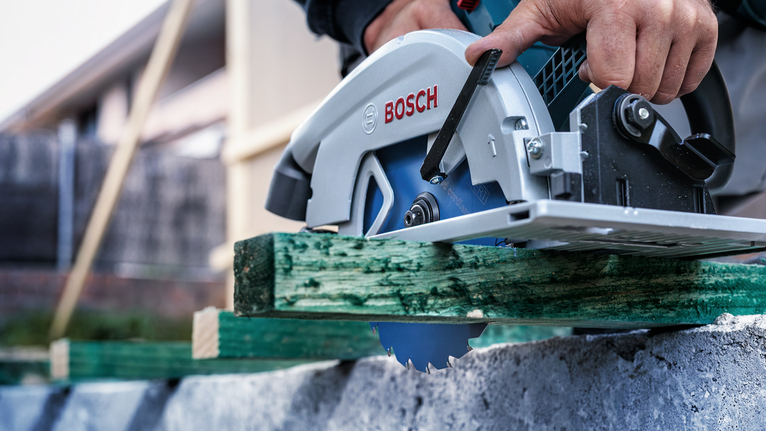 佩戴安全设备的人员使用圆锯切割绿色木材。.