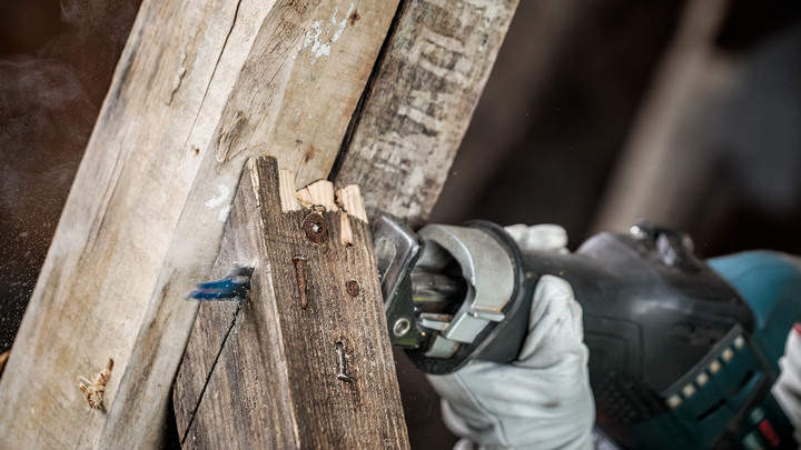 佩戴安全设备的人员使用往复锯切割木梁。.