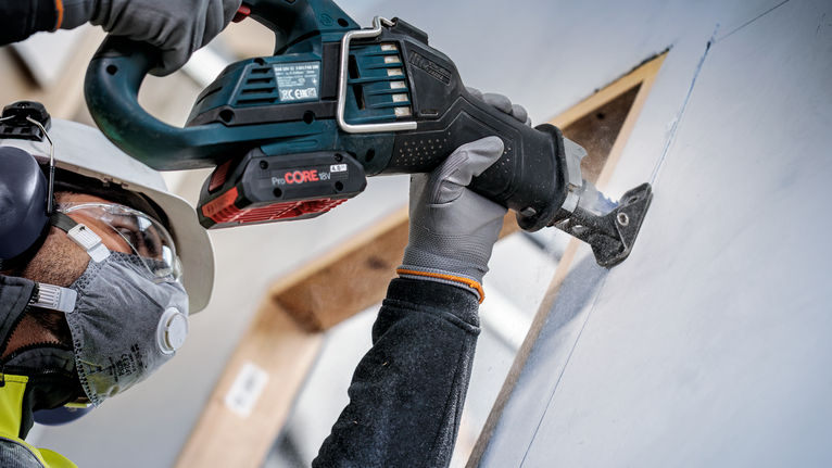 佩戴安全设备的人员使用往复锯切割干墙。.