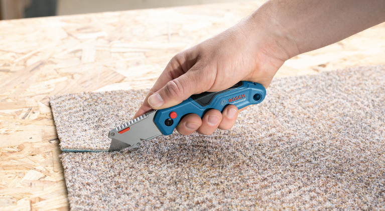 有人在木质表面上用美工刀切割地毯。