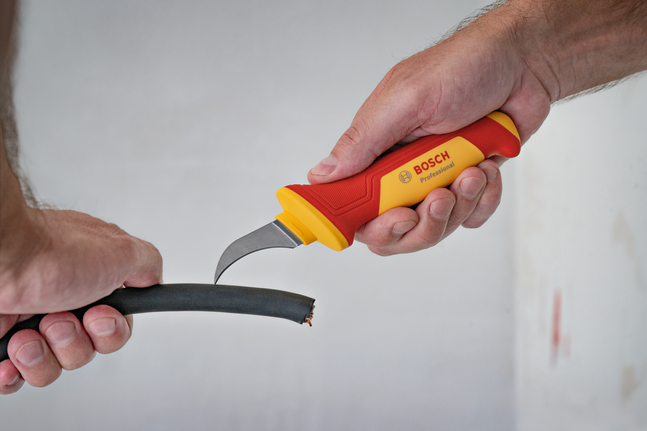 有人用绝缘刀剥去粗电缆的外层绝缘层。