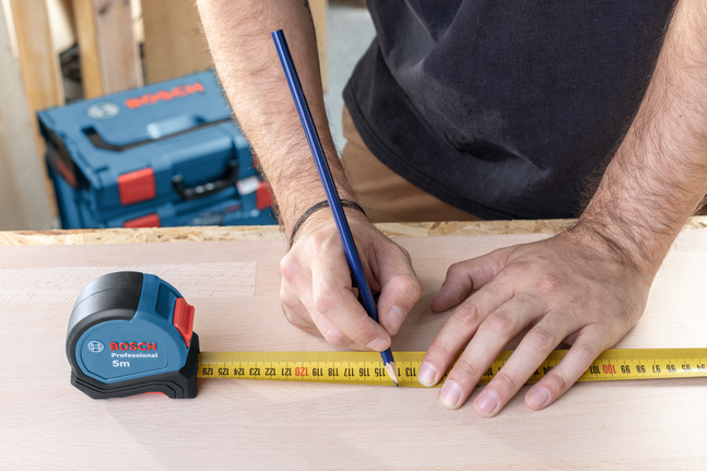 有人用卷尺和铅笔在木头上做测量标记。