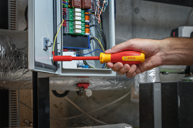 有人使用绝缘螺丝刀调整电气控制面板内的线路。