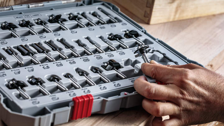 一名工人从木制工作台上整齐排列的盒子中挑选路由器钻头。.