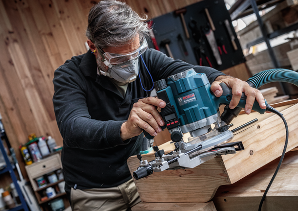 佩戴安全设备的人员使用路由器来塑造木板的边缘。.