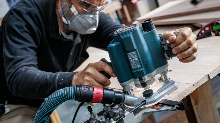 佩戴安全设备的人员使用电动铣刀来修整木板的边缘。.