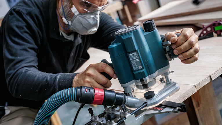 佩戴安全设备的人员使用电动铣刀来修整木板的边缘。.