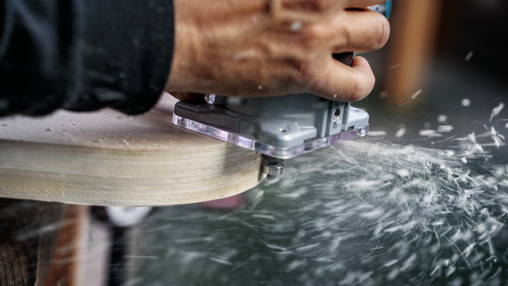 当刨花散落时，人员引导电动工具沿着木材边缘移动。.