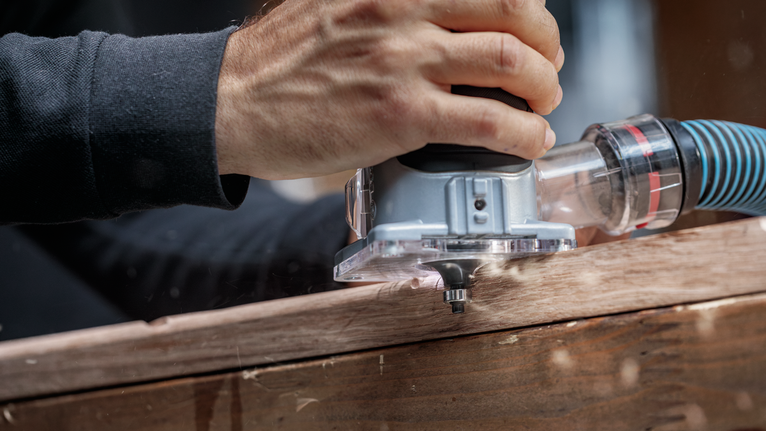 人员引导电动铣刀沿着木板进行精确的边缘修整。.