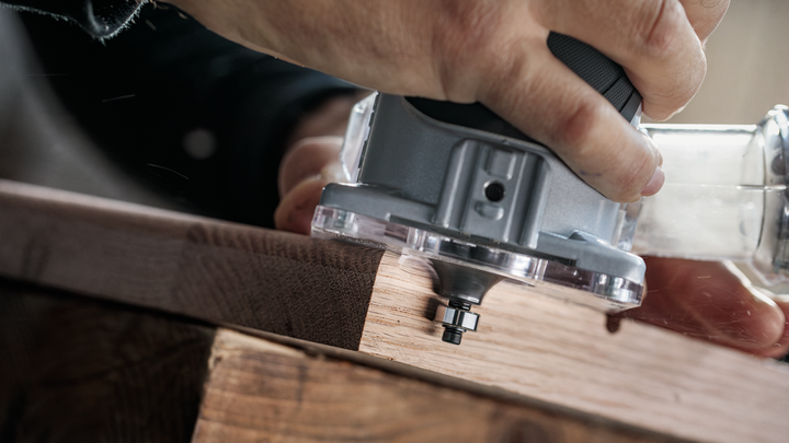 一名男子正操作电动修边机沿着木板边缘修整。.