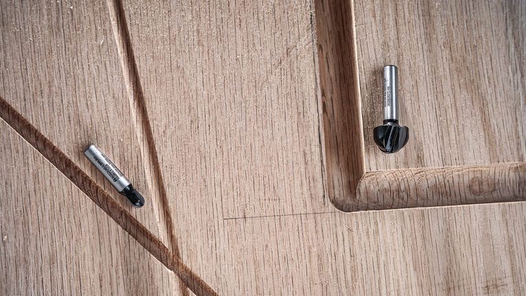两个路由器钻头放在带有凹槽细节的雕刻木质表面上。.
