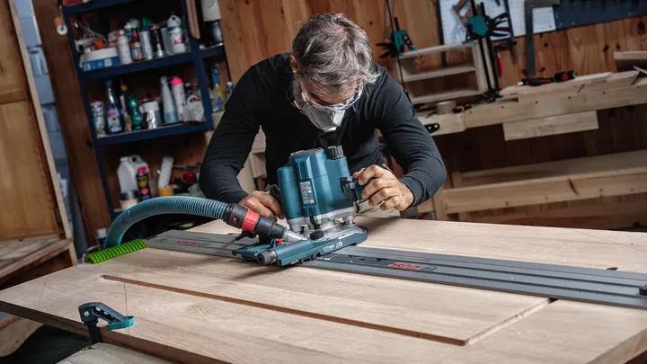 佩戴安全设备的人员引导路由器沿着轨道塑造木板。.