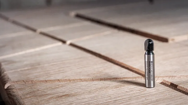 金属路由器钻头直立在有凹槽的木质表面上。.