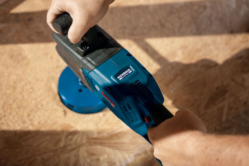 一个人在木质表面上操作蓝色无绳角钻。.