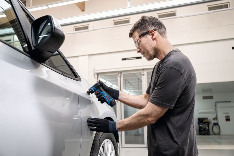 一名佩戴安全设备的人员正在使用轨道砂光机打磨车门。