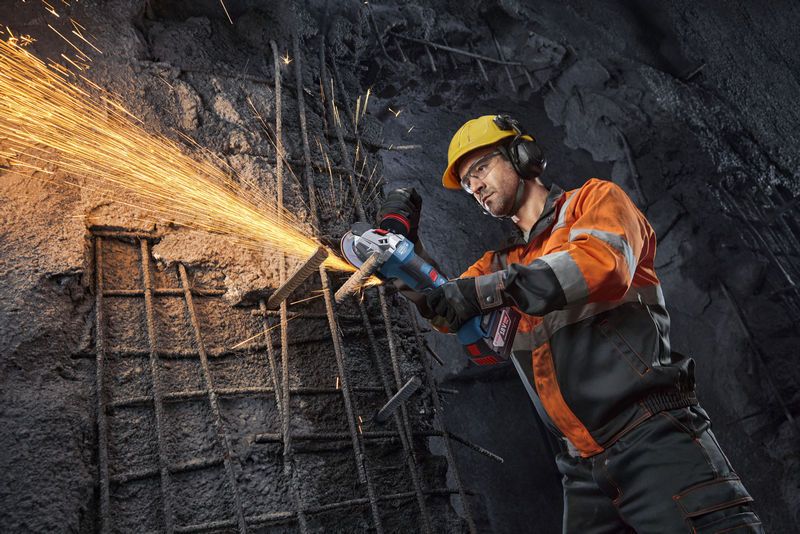 一名佩戴安全装备的人员使用角磨机切割钢筋，产生火花。