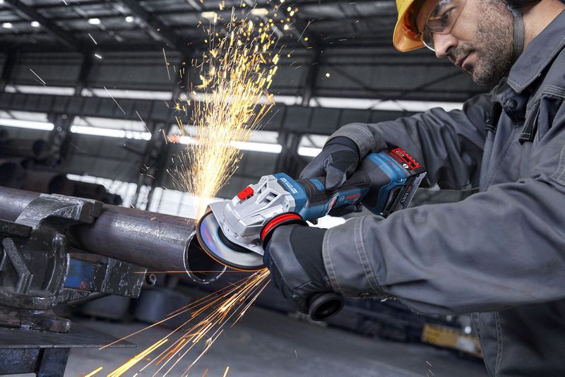 一名佩戴安全装备的人员用角磨机打磨金属管，产生火花。