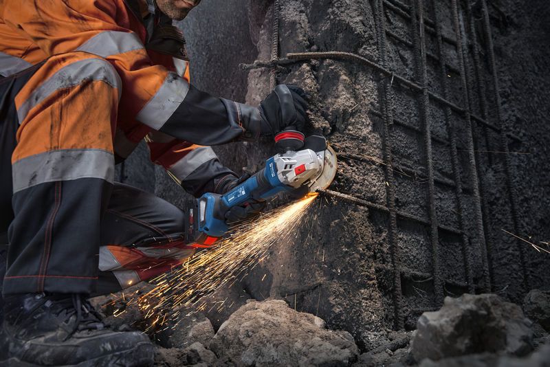 一名佩戴安全装备的人员使用角磨机切割混凝土，产生火花。