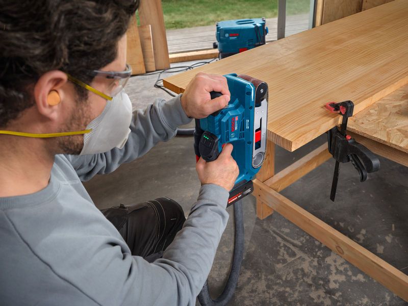 一名佩戴安全装备的人员正在使用带式砂光机打磨木板。