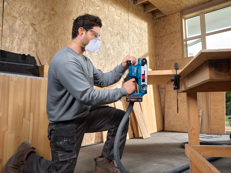 一名佩戴安全装备的人员正在使用带式砂光机打磨木板。