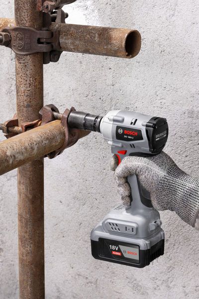 一名佩戴安全设备的人员使用无绳冲击扳手拧动金属管道。.