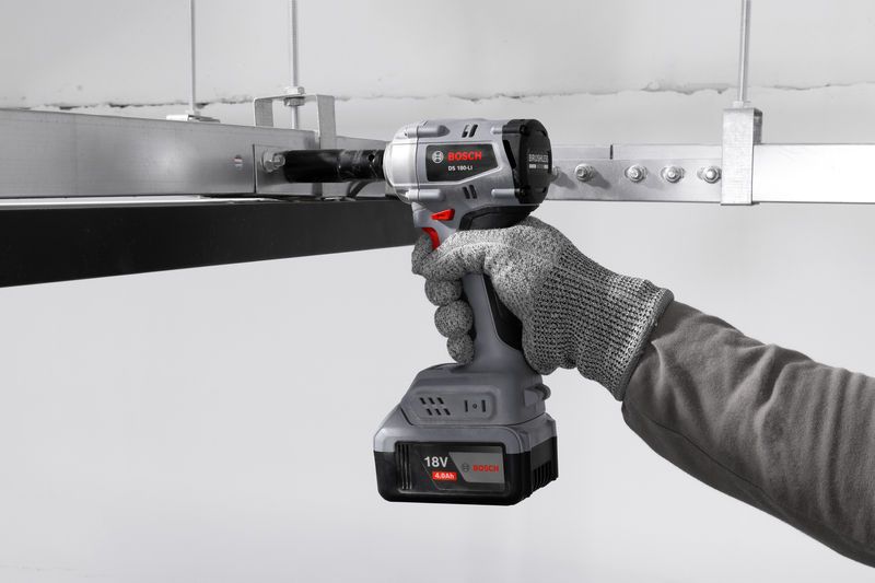 一名佩戴安全设备的人使用无绳冲击扳手紧固金属框架。.