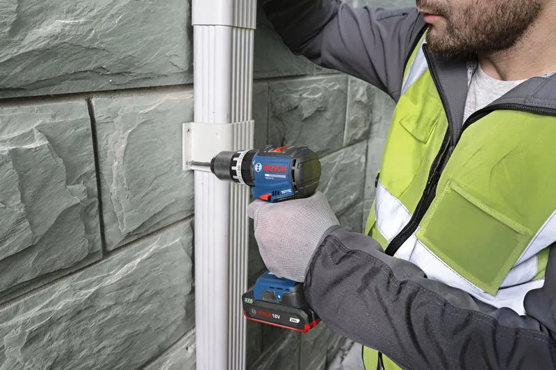 一名佩戴安全装备的人员使用无绳电钻将支架固定在墙上。