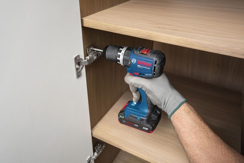 一名佩戴安全装备的人员使用无绳冲击钻安装橱柜铰链。