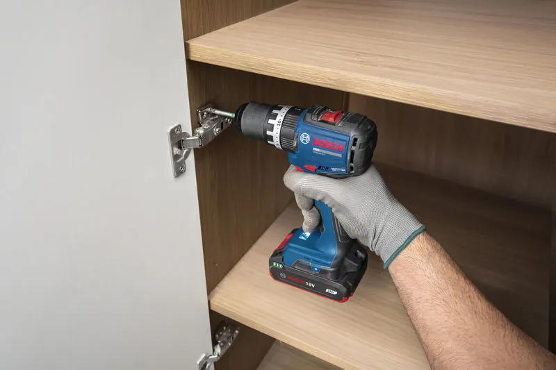 一名佩戴安全装备的人员使用无绳冲击钻安装橱柜铰链。