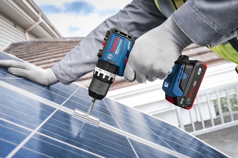 一名佩戴安全装备的人员使用无绳冲击钻将支架固定到太阳能电池板上。