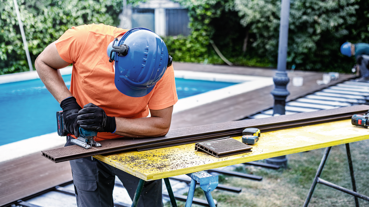 佩戴安全设备的人员使用曲线锯在户外切割甲板板。.