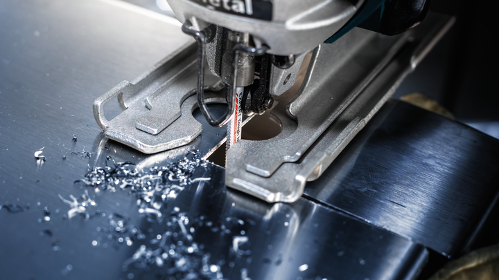 拼图锯切割一块金属板，小金属屑散落在刀片周围。.