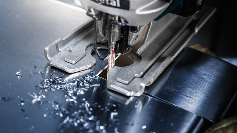 拼图锯切割一块金属板，小金属屑散落在刀片周围。.