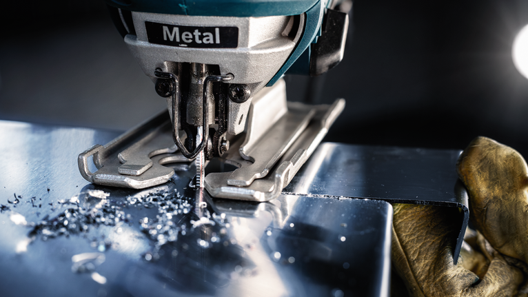 佩戴安全设备的人员使用曲线锯切割金属板。.