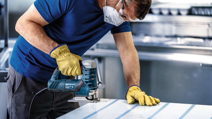 佩戴安全设备的人员使用曲线锯切割金属板。.