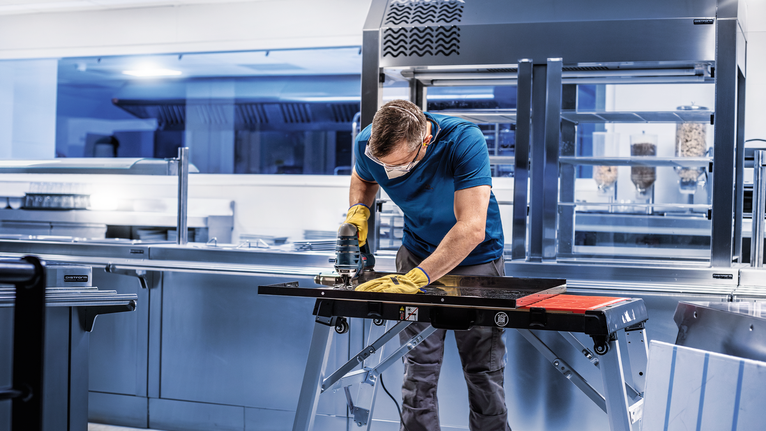 一名佩戴安全设备的人员在厨房的工作台上打磨金属板。.