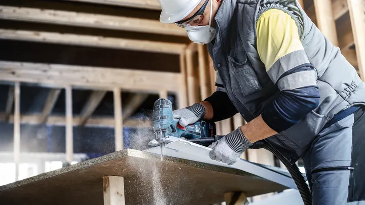 佩戴安全设备的人员在施工区域使用电动工具切割木板。.