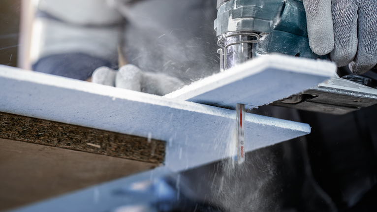 佩戴安全设备的人员使用电动曲线锯切割泡沫绝缘板。.