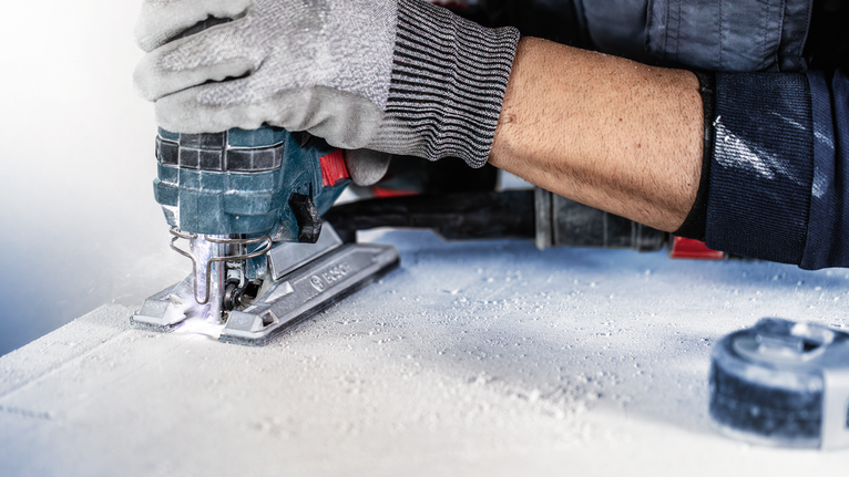 佩戴安全设备的人员使用曲线锯切割一片材料。.