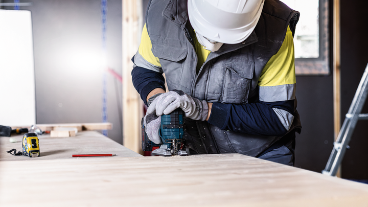 佩戴安全设备的人员使用电动工具在工作台上切割木材。.