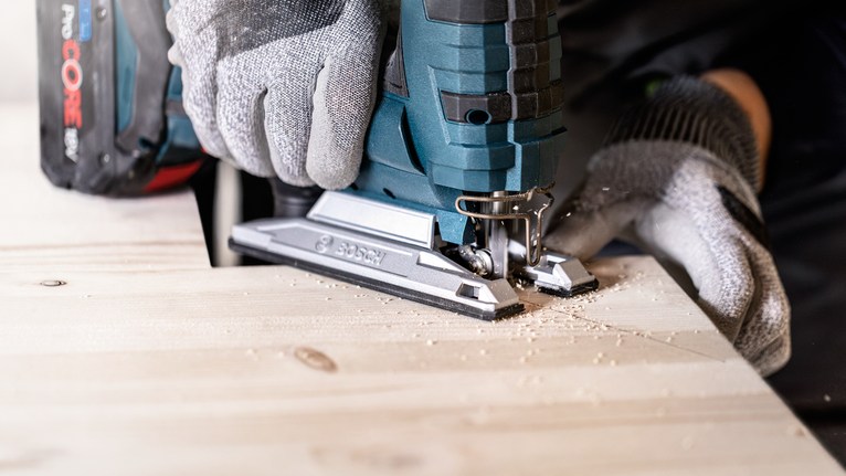 佩戴安全设备的人员使用无绳曲线锯切割木板。.