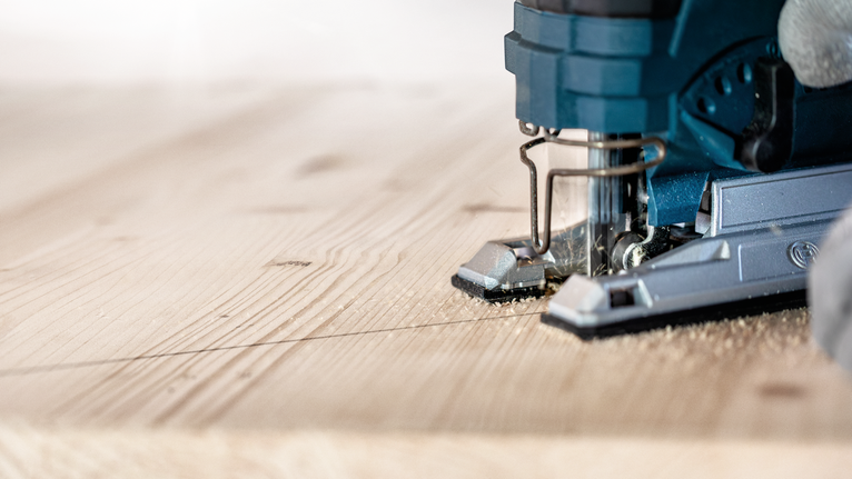 一个人引导拼图沿着标记线切割木板。.