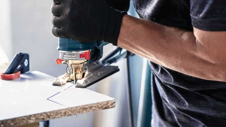 佩戴安全设备的人员用拼图锯切割标记的木板。.