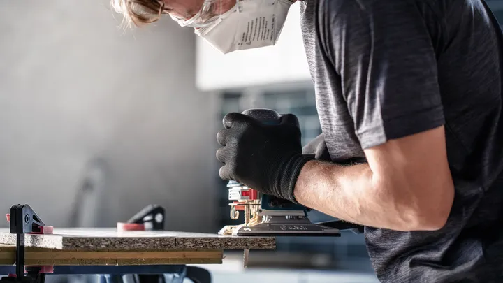 佩戴安全设备的人员使用电动工具切割木材。.